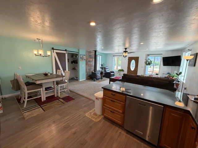Open-concept living area featuring wood-finish flooring throughout, stainless steel appliances, and wood cabinetry with dark countertops