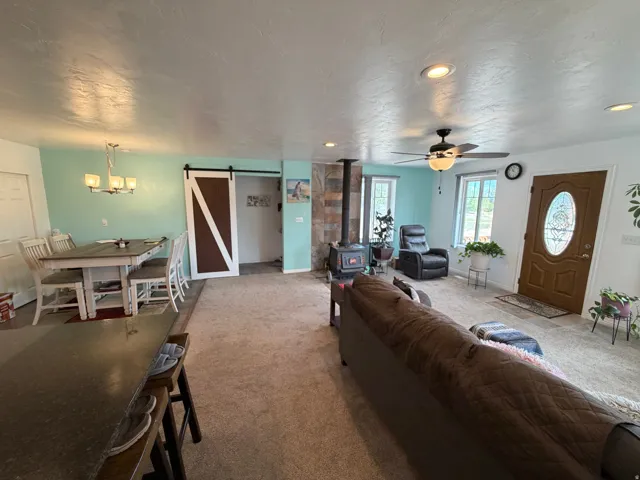Recessed ceiling lighting, wood-burning stove with stone surround, ceiling fan, wood-finish front door with oval glass insert, and a sliding barn-style door