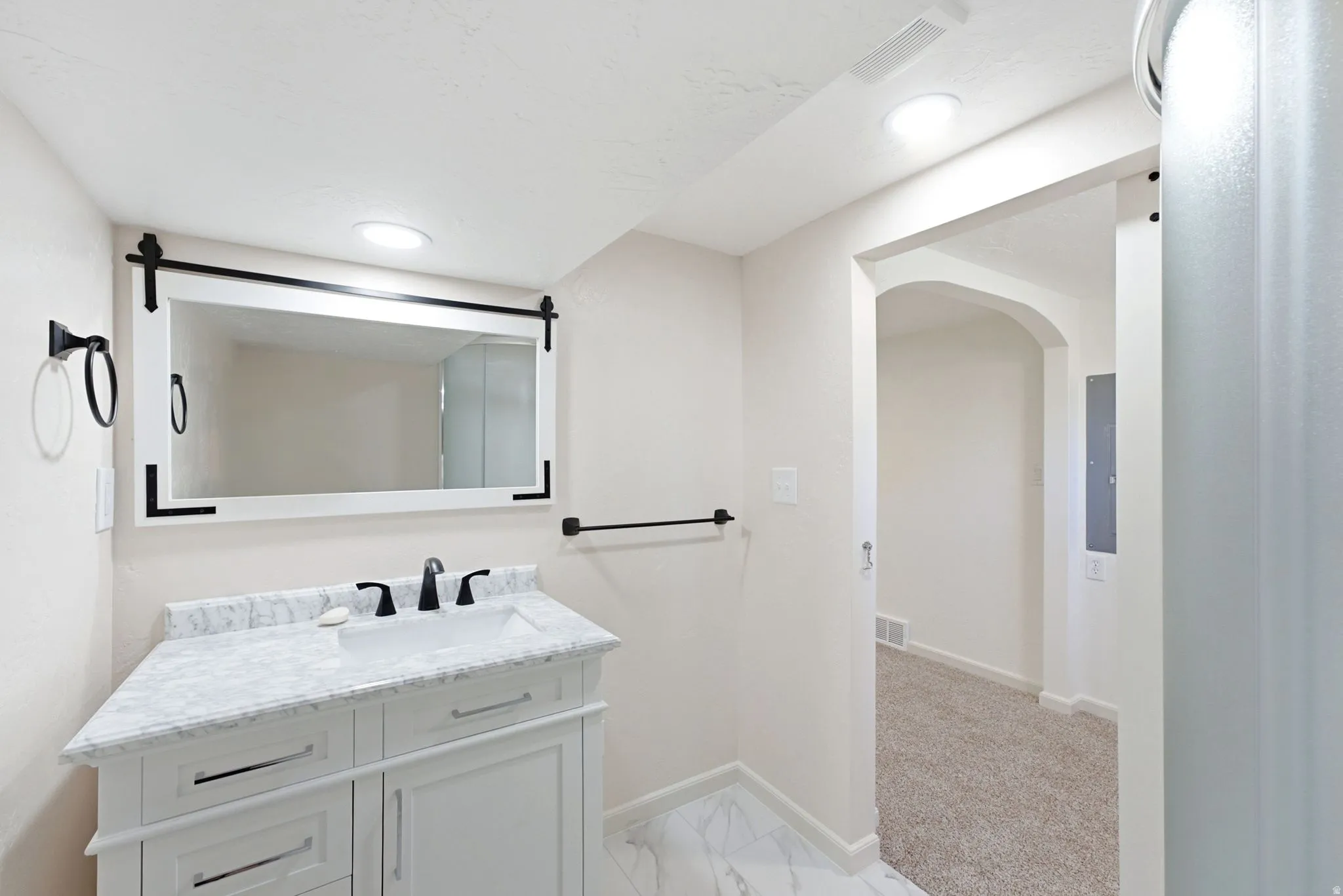 White vanity with a built-in sink, stone countertop, matte black faucet, and a wall-mounted mirror with black hardware