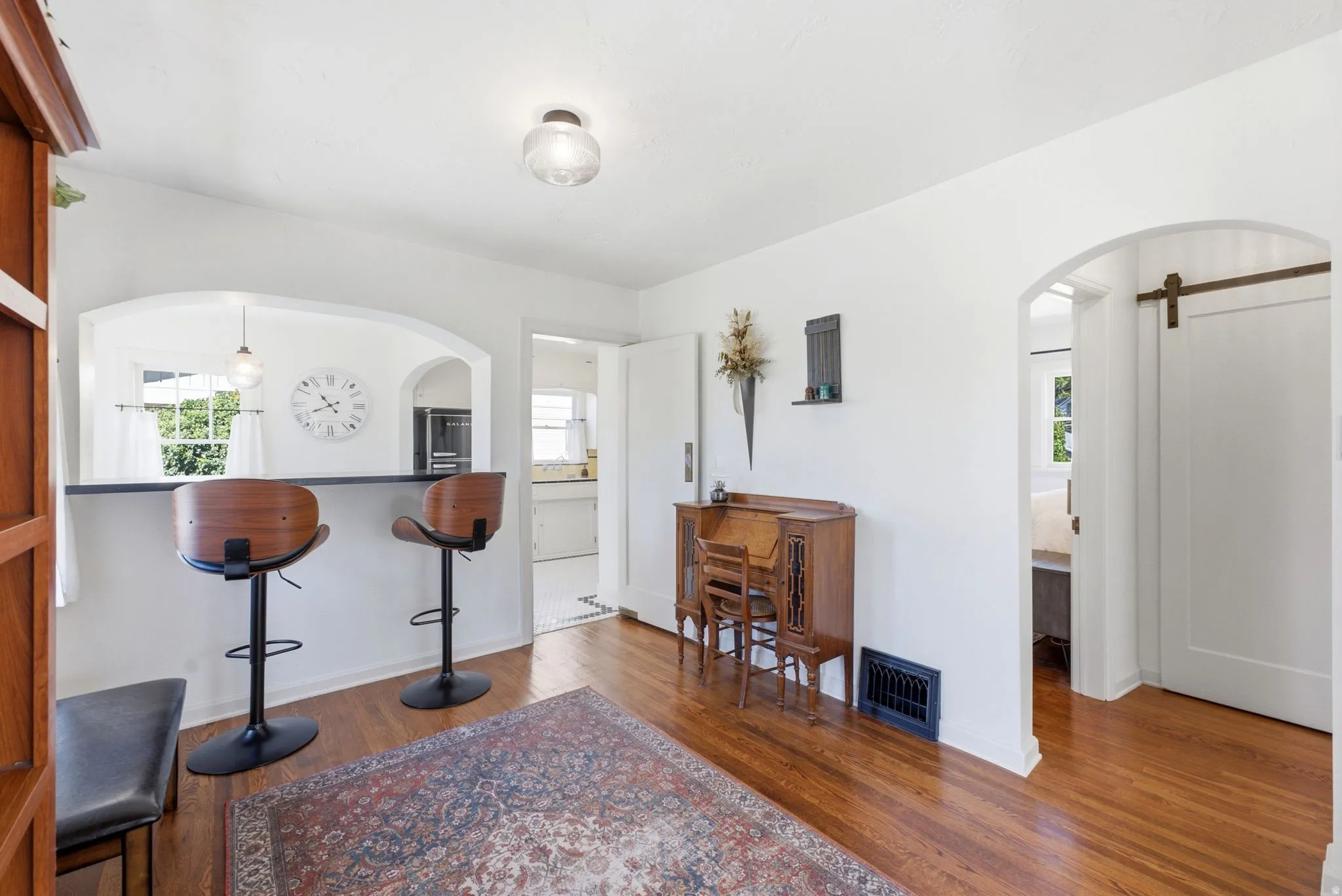 Hardwood flooring, arched doorways, a built-in breakfast bar with a solid surface countertop, recessed lighting, and a barn door entry