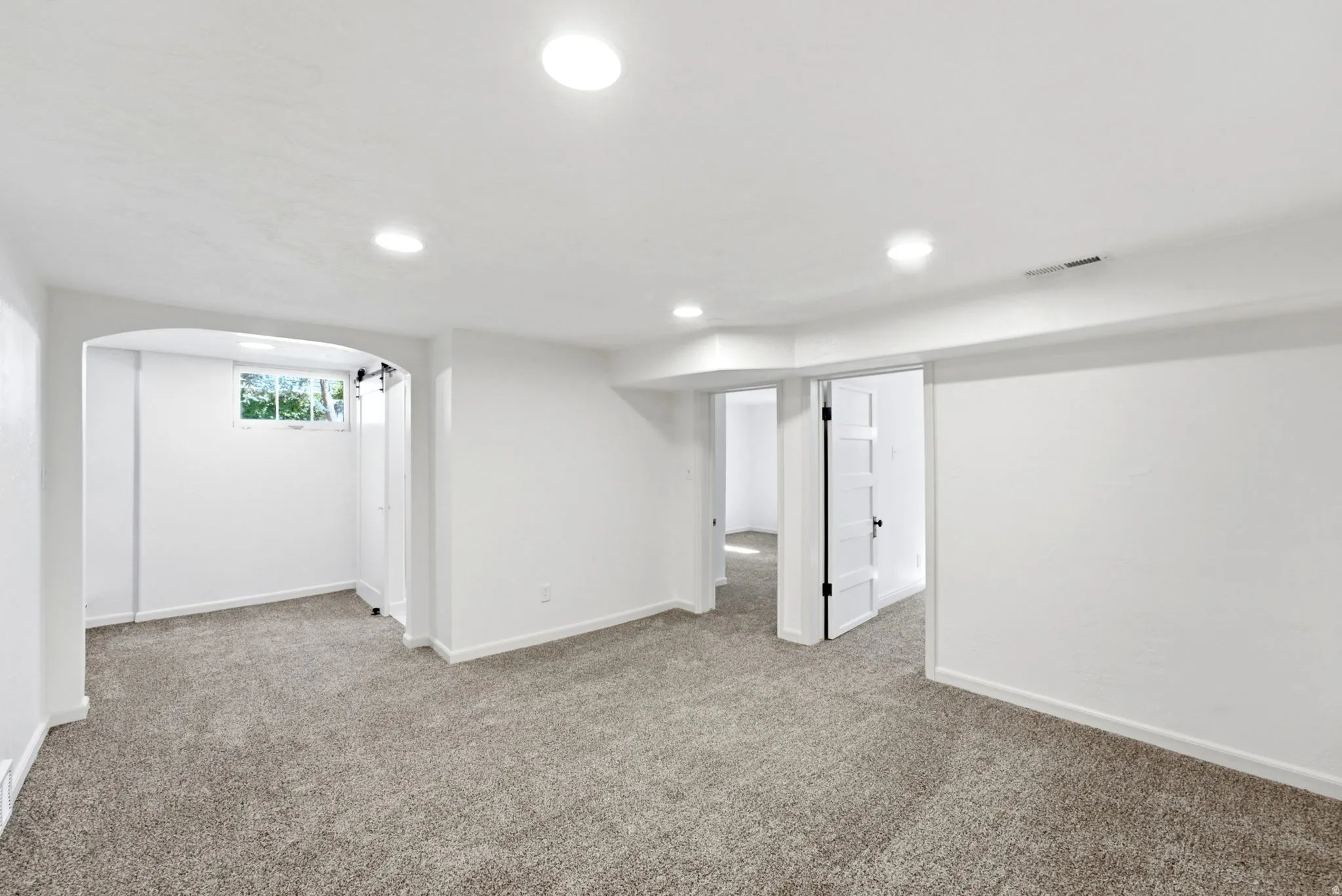 Recessed lighting, light-colored carpeting, white interior walls, and an arched doorway
