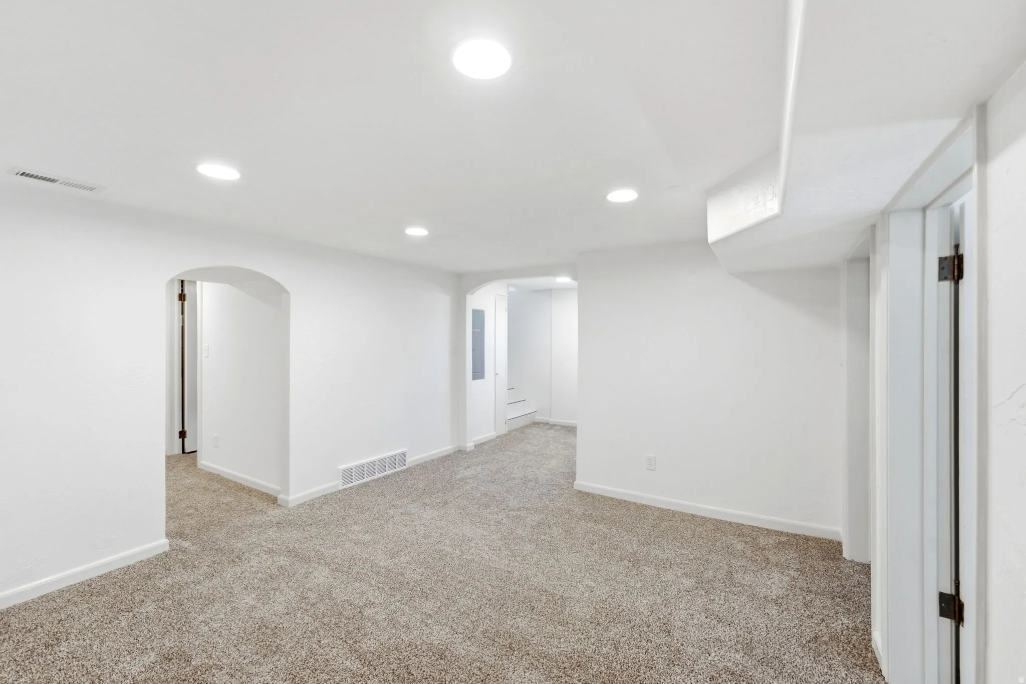 Recessed lighting illuminates the carpeted flooring and white walls, featuring arched doorways and a white door frame