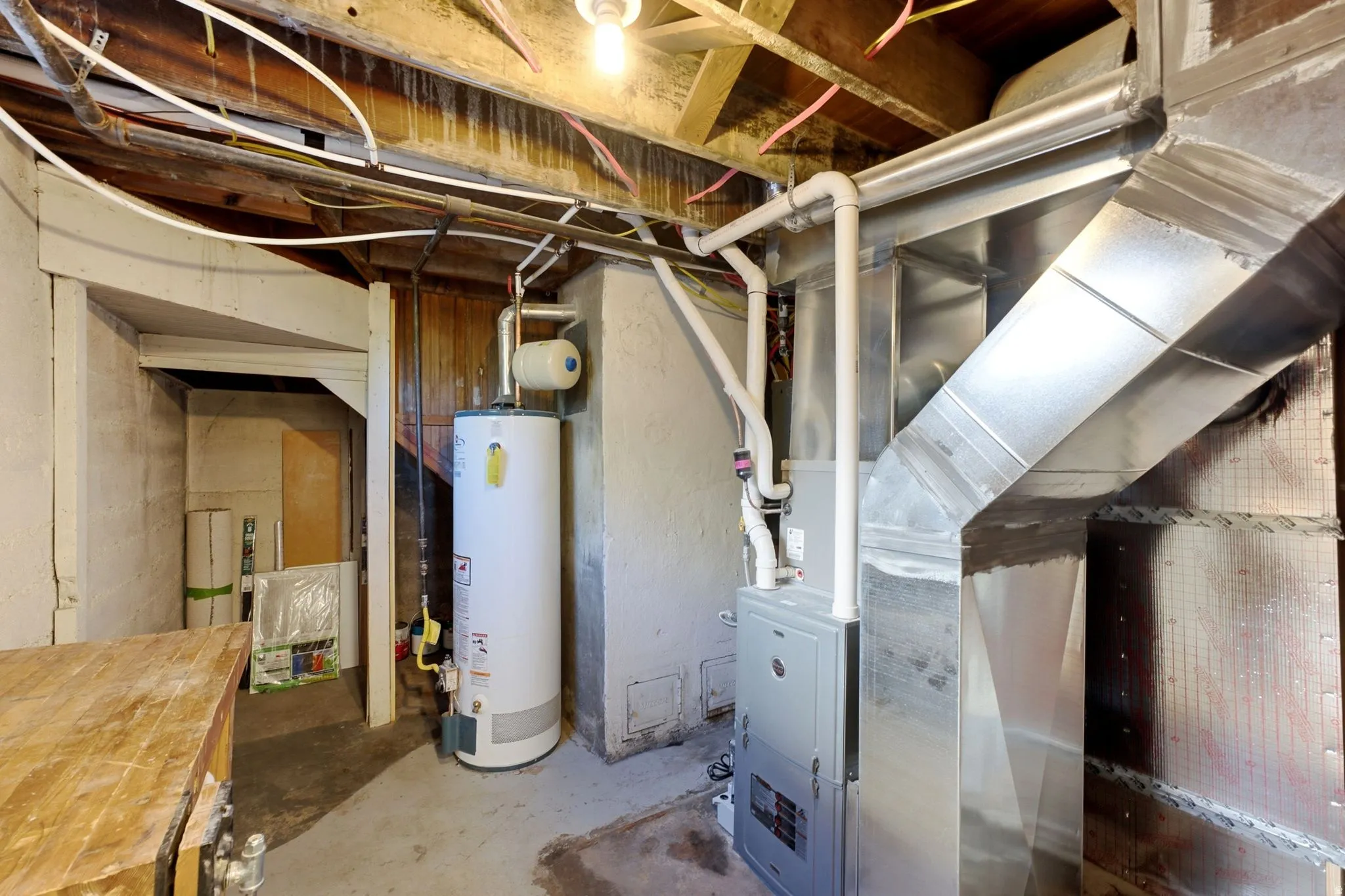Exposed ceiling joists with visible electrical and plumbing lines, concrete flooring, and a water heater