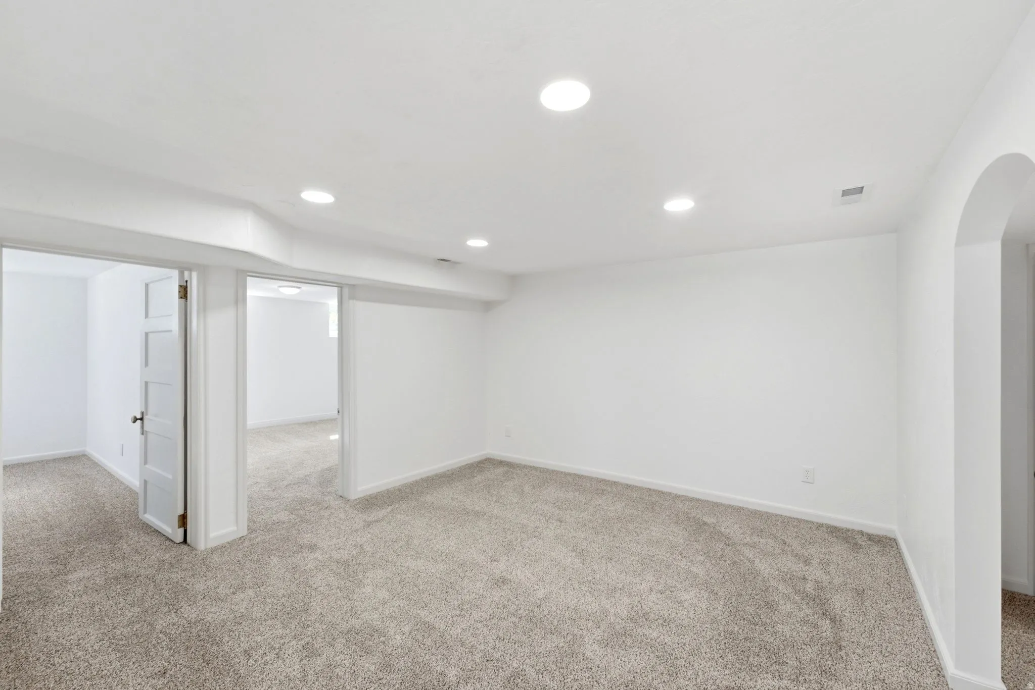 Recessed ceiling lighting, light gray carpeting, white walls, and an arched doorway