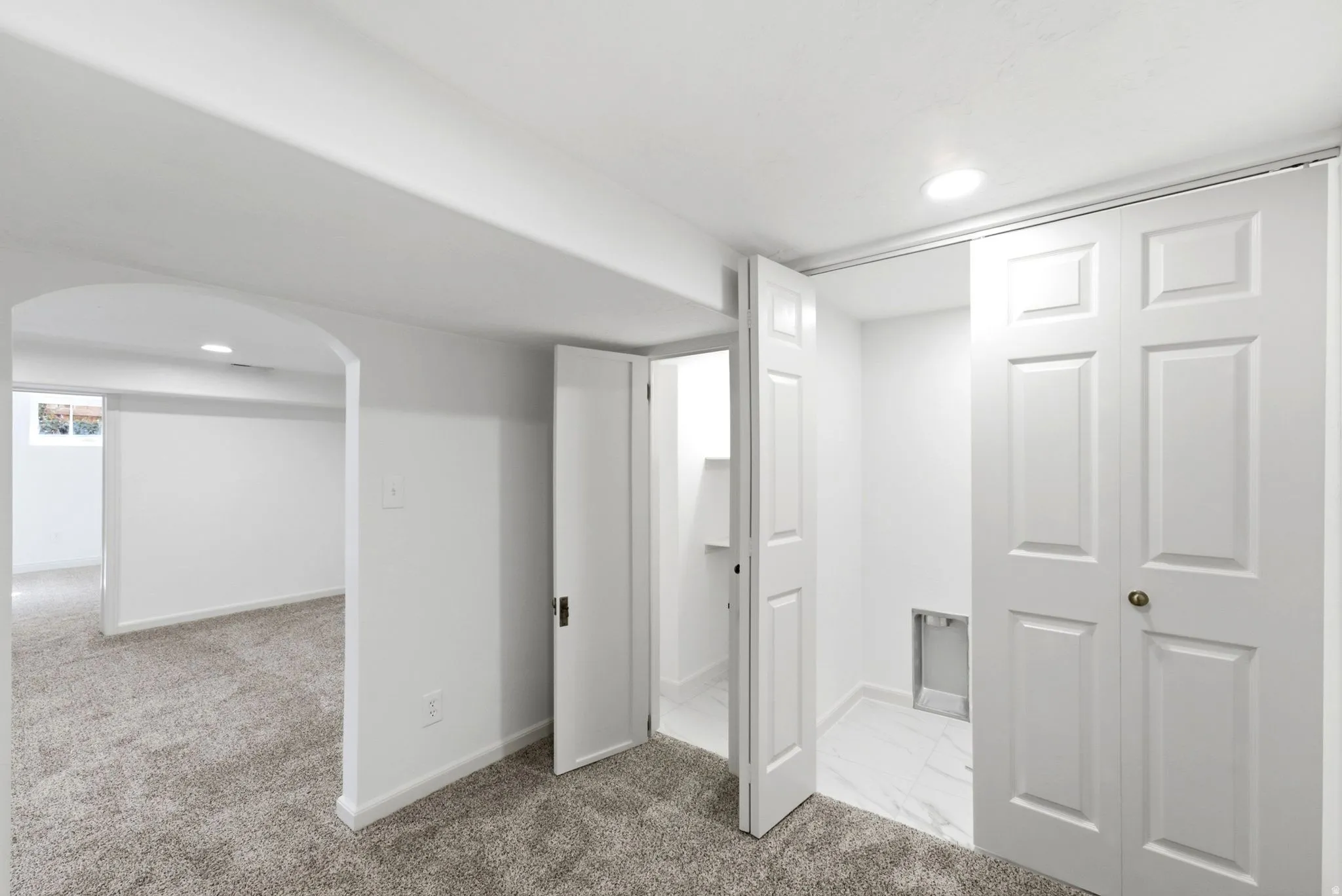Arched doorway, recessed lighting, gray carpeting, white bifold doors, and white paneled doors