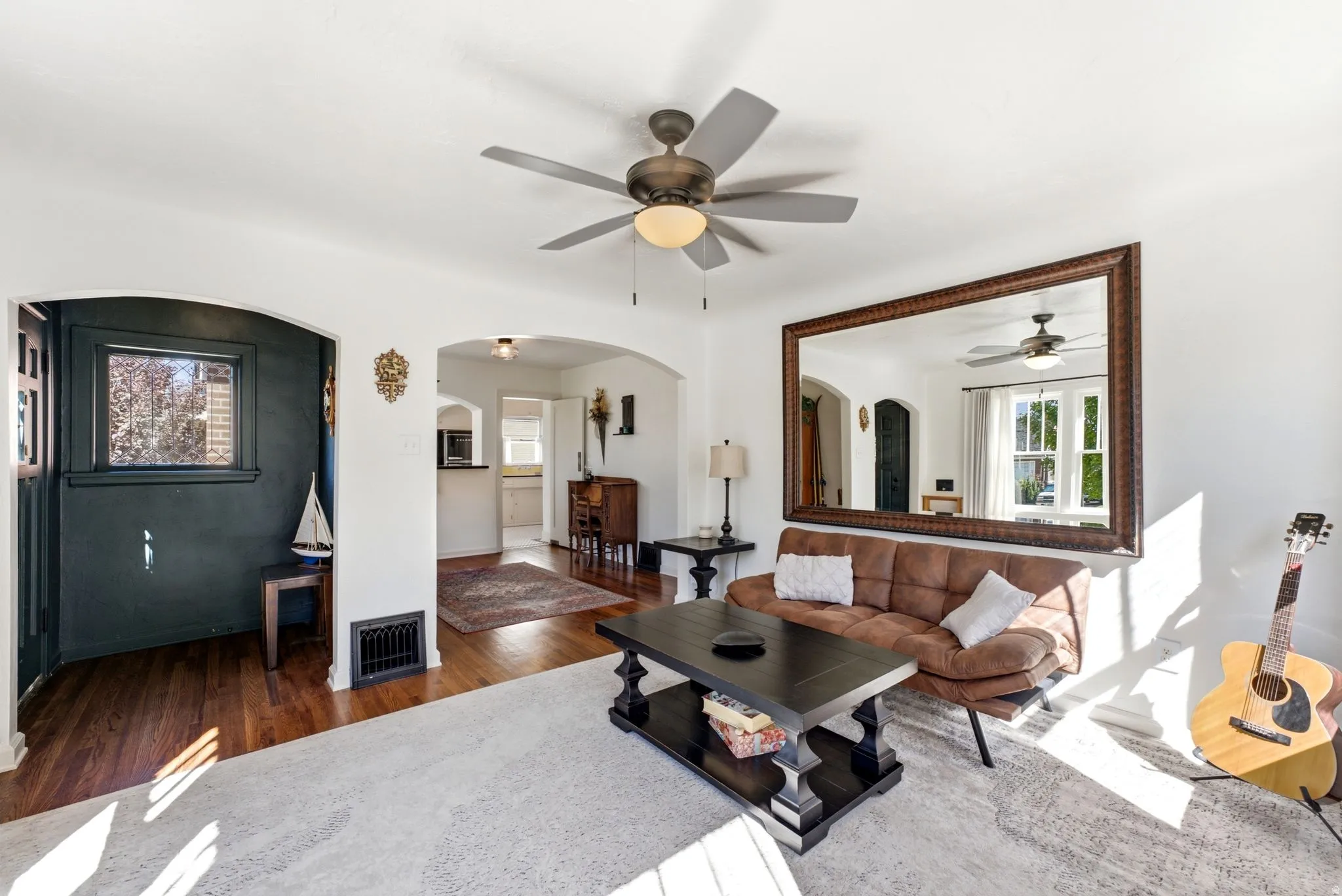 Hardwood-finish flooring, arched doorways, a ceiling fan with integrated lighting, and a large wall-mounted mirror
