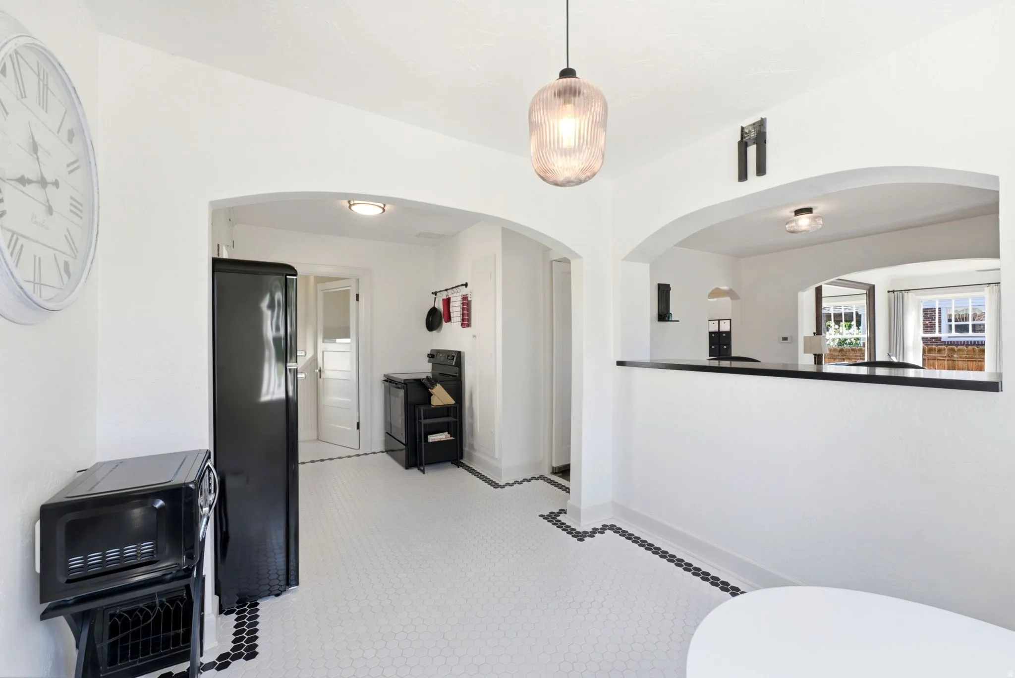 White hexagon tile flooring with black accent border, arched doorways, and a black countertop pass-through
