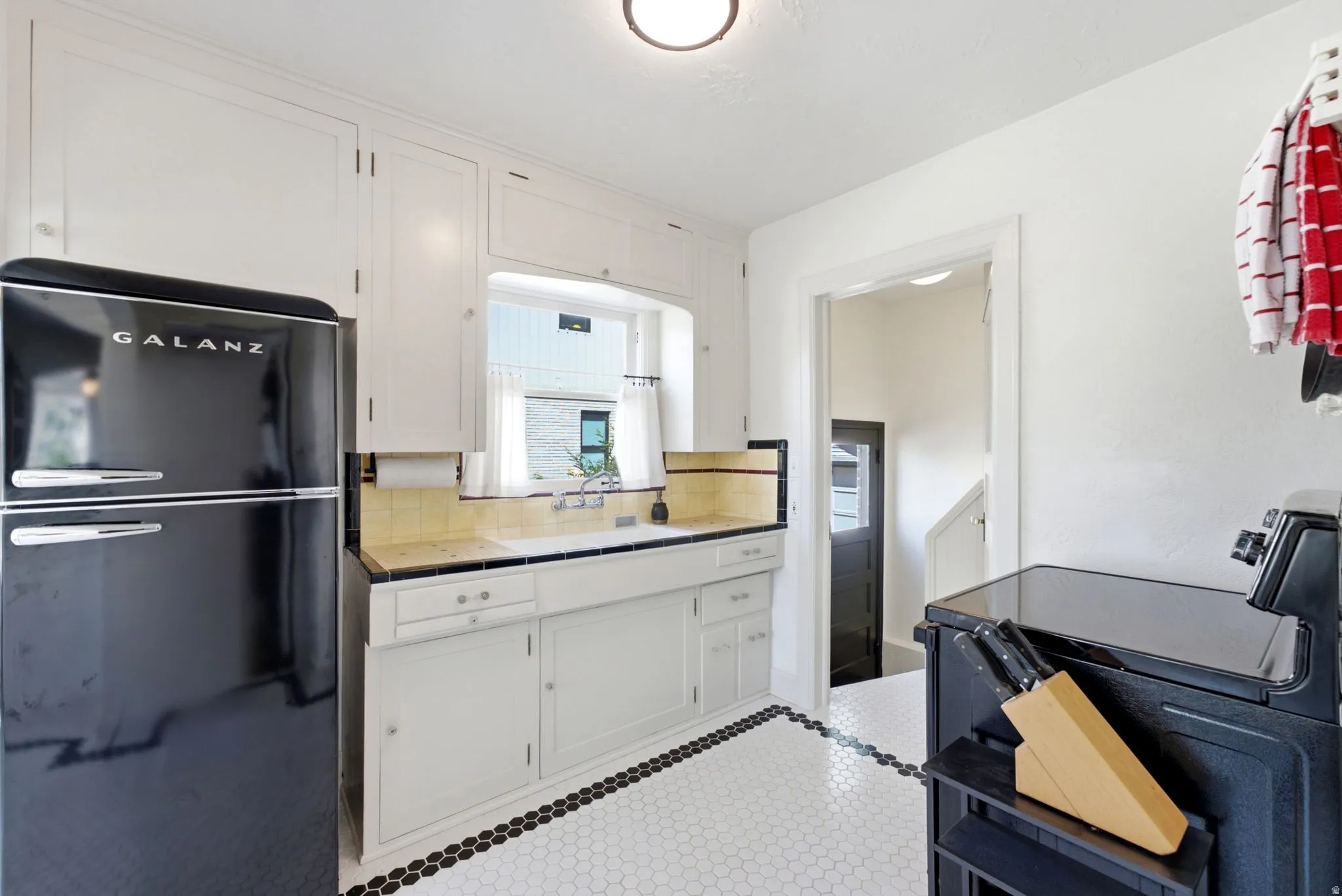 Kitchen featuring white cabinetry, a black retro-style refrigerator, a built-in sink, and hexagonal tile flooring with a contrasting border