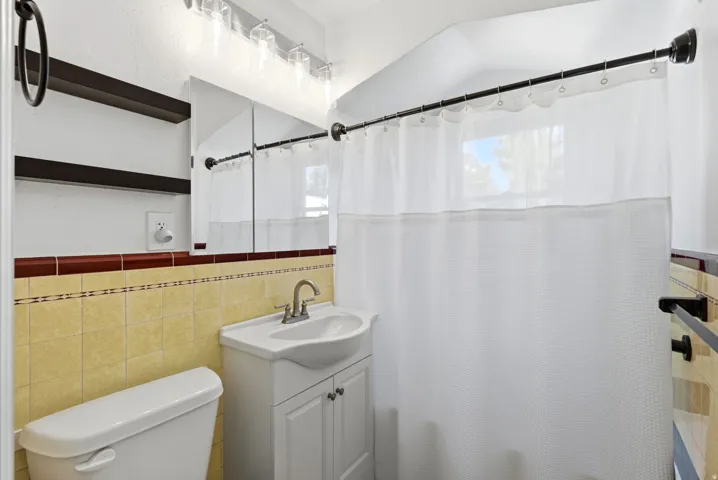 Bathroom featuring a single vanity, wall-mounted medicine cabinet, overhead lighting, and tiled walls with a decorative border