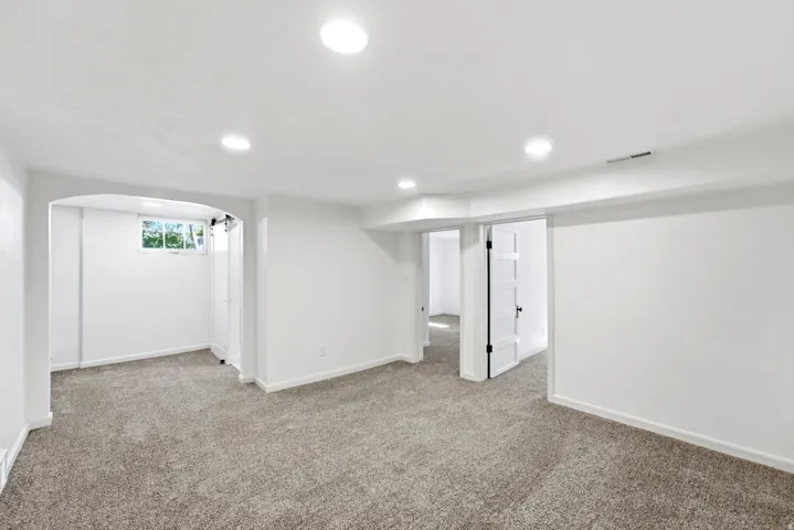 Recessed lighting, light-colored carpeting, white interior walls, and an arched doorway