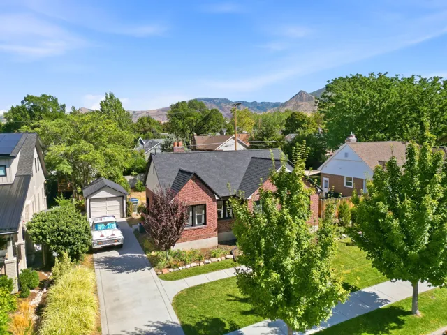 Brick exterior with black roof, attached garage, and landscaped front yard with mature trees