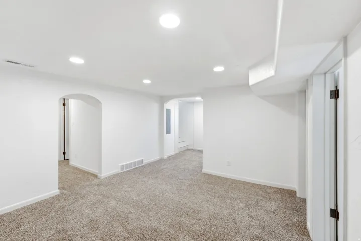 Recessed lighting illuminates the carpeted flooring and white walls, featuring arched doorways and a white door frame