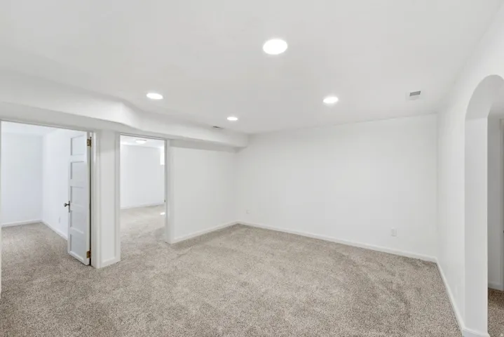 Recessed ceiling lighting, light gray carpeting, white walls, and an arched doorway