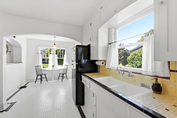 Kitchen with white shaker cabinetry, dual-basin sink, yellow tiled backsplash, and black and white hexagon tile flooring