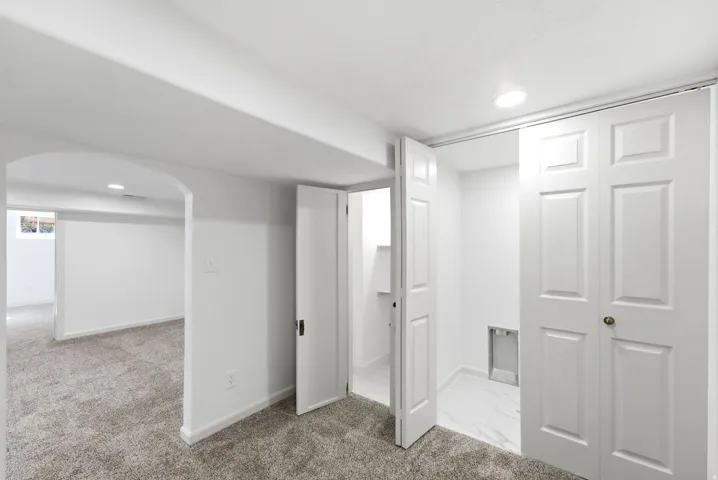 Arched doorway, recessed lighting, gray carpeting, white bifold doors, and white paneled doors