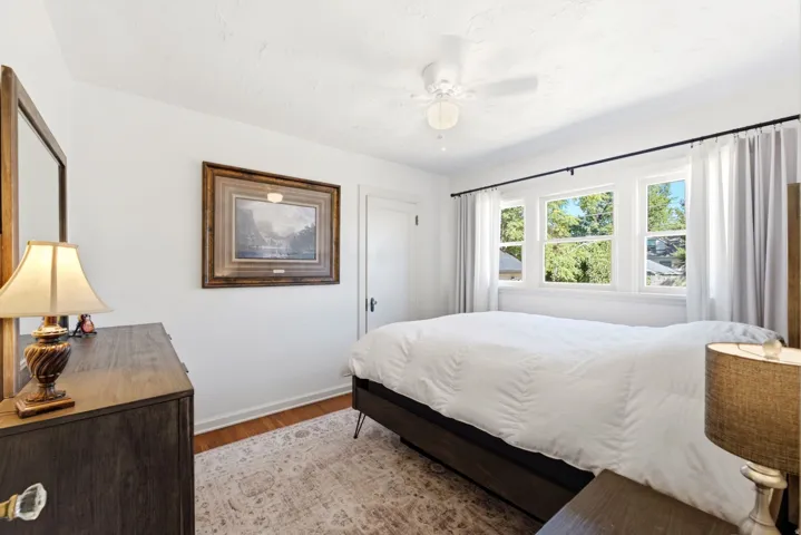 White ceiling fan with integrated lighting, wood-finish flooring, white walls, and a window with three distinct panes