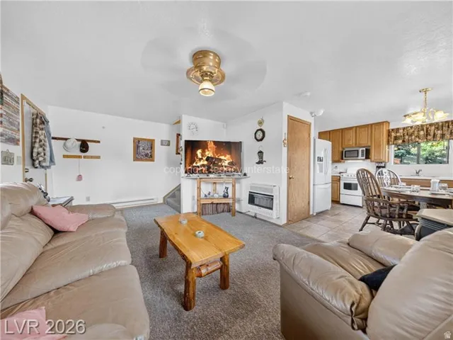 Open-concept living area with a ceiling fan, wall-mounted heater, and carpeted flooring
