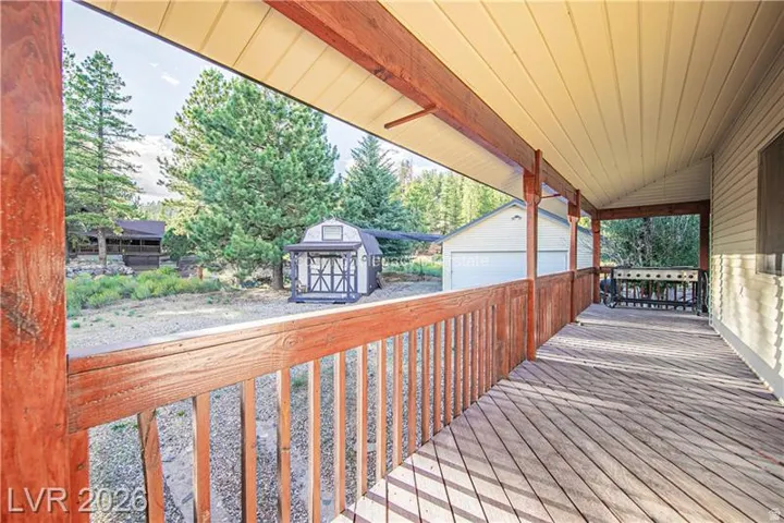 Expansive covered porch with wood railing and decking, offering a broad perspective of the surrounding natural landscape