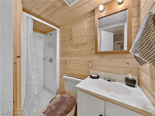 Wood-paneled bathroom featuring a corner vanity with an integrated sink, a built-in shower stall, and a wood-framed mirror with overhead lighting