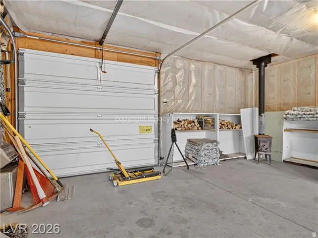 Finished concrete floor, white insulated garage door, wood-burning stove, built-in shelving, and wood paneling