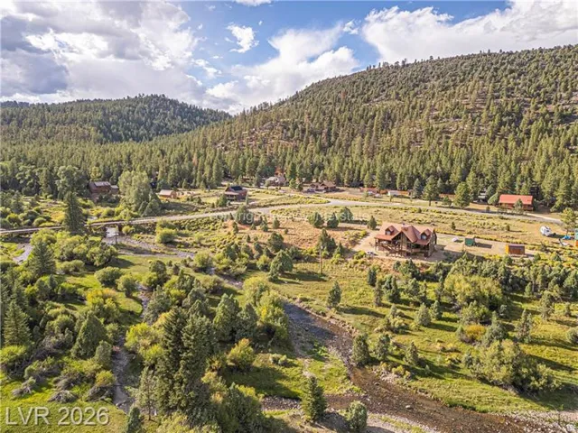 Multiple structures nestled within a verdant valley, surrounded by dense evergreen forests and rolling hills