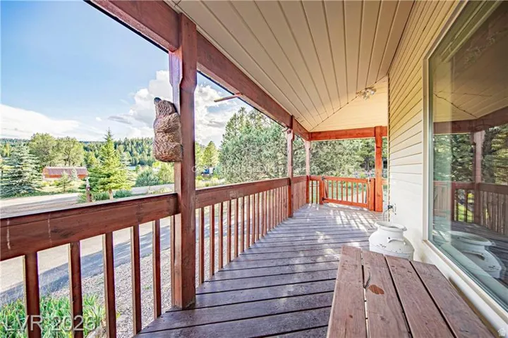 Covered porch featuring a wood-plank floor, wooden railing, and a window with a reflective surface