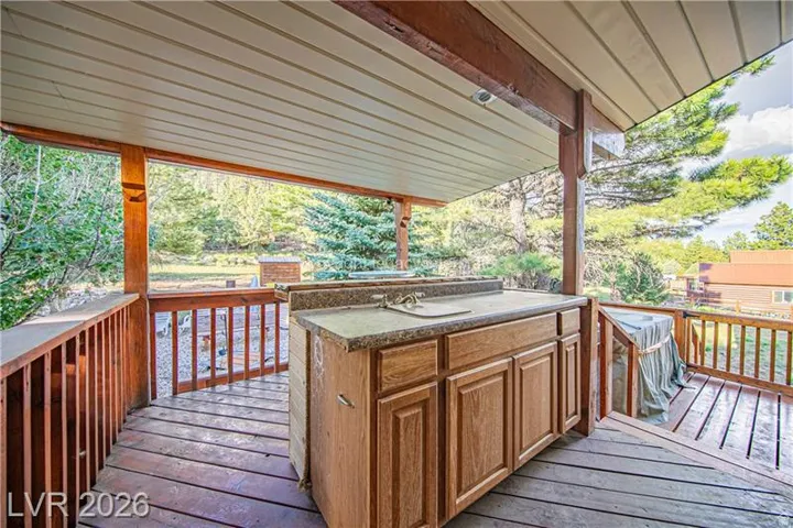 Covered outdoor deck with a built-in outdoor kitchen featuring a sink, wood cabinetry, and a stone-finish countertop