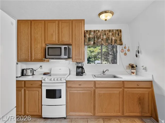Wood-finish cabinetry, white countertops, stainless steel sink, and white oven range