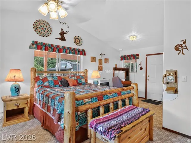 Vaulted ceiling with ceiling fan and light fixture, window with valance, light-toned wall color, and wood-finish flooring