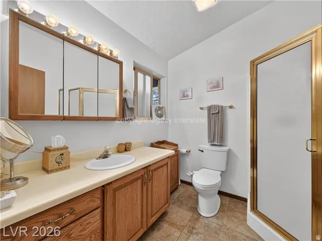 Bathroom featuring a wood-finish vanity with an integrated sink, a large mirrored medicine cabinet, a full toilet, a glass-enclosed shower, and tile flooring