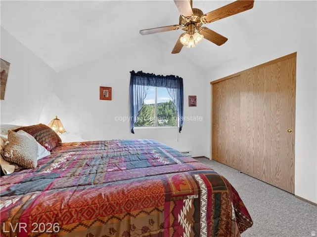Vaulted ceiling with a ceiling fan, window with exterior scenery, wood-finish sliding closet doors, and light-colored carpet