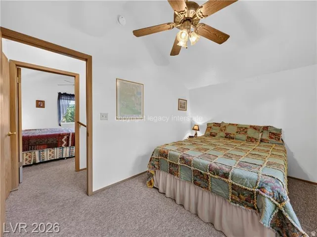 Vaulted ceiling with a ceiling fan, neutral wall paint, and plush carpeting throughout