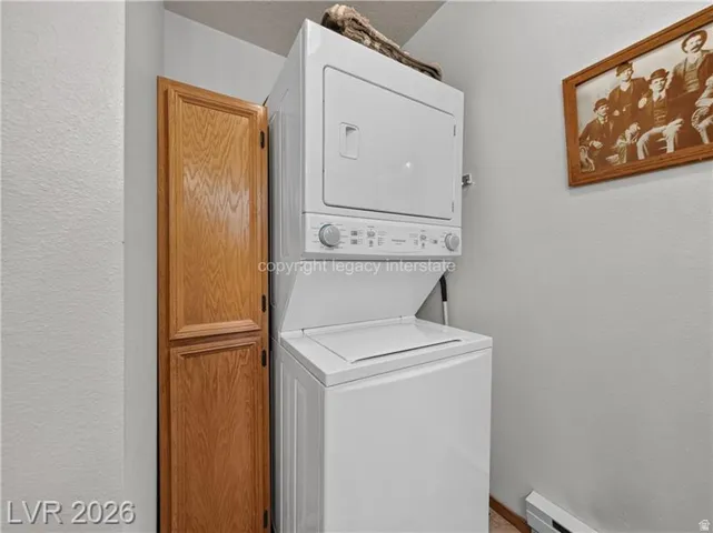 Stackable white washer and dryer unit, light wood-finish storage cabinet, and light-colored walls