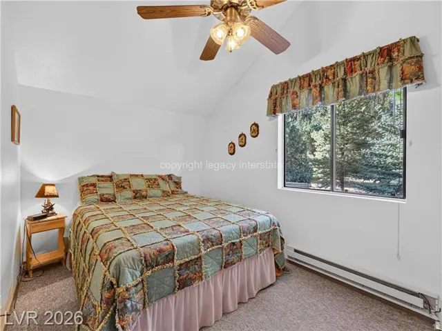 Vaulted ceiling with a ceiling fan, carpeted flooring, and a large window with outdoor scenery