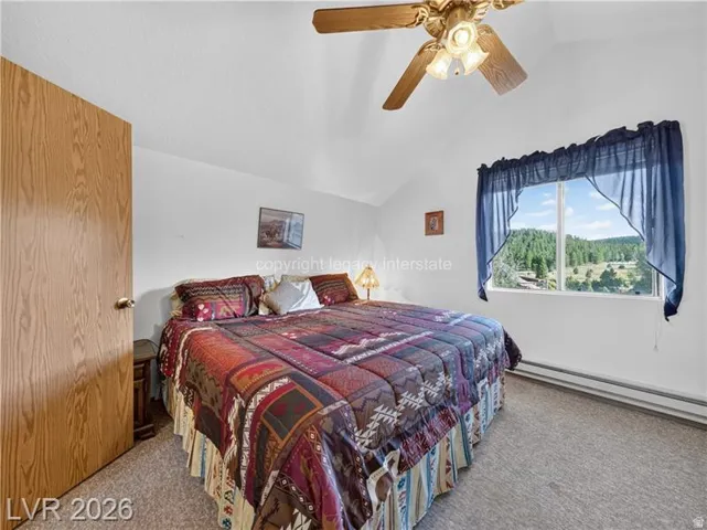 Sloped ceiling with an attached ceiling fan and light fixture, wood-finish door, large window, and carpeted flooring