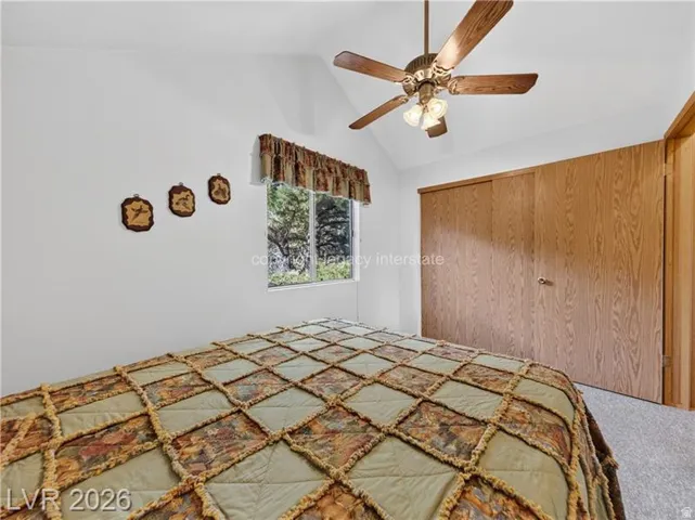 Vaulted ceiling featuring a ceiling fan with integrated lighting, wood-finish closet doors, and carpet flooring