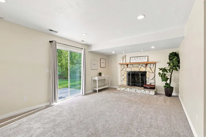 Stone-faced fireplace with a wood mantel, sliding glass door, recessed lighting, and light-toned carpeting