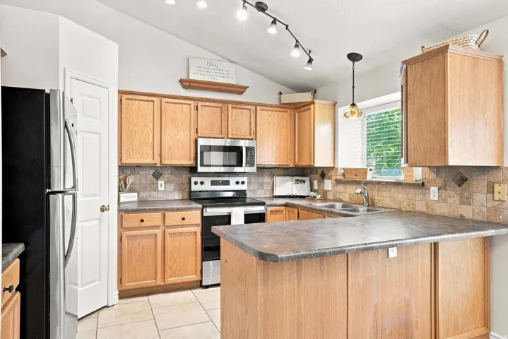 Vaulted ceiling kitchen featuring wood-finish cabinetry, stainless steel appliances, stone-look countertops, and tile flooring