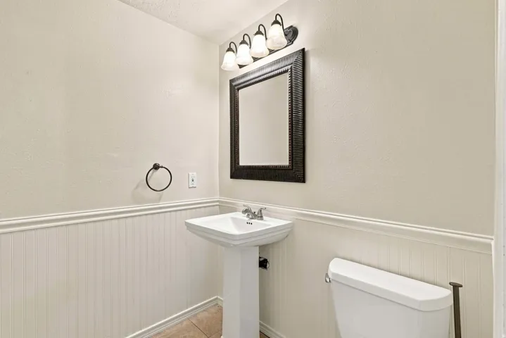 Pedestal sink with chrome faucet, beadboard wainscoting, framed mirror, and wall-mounted light fixture