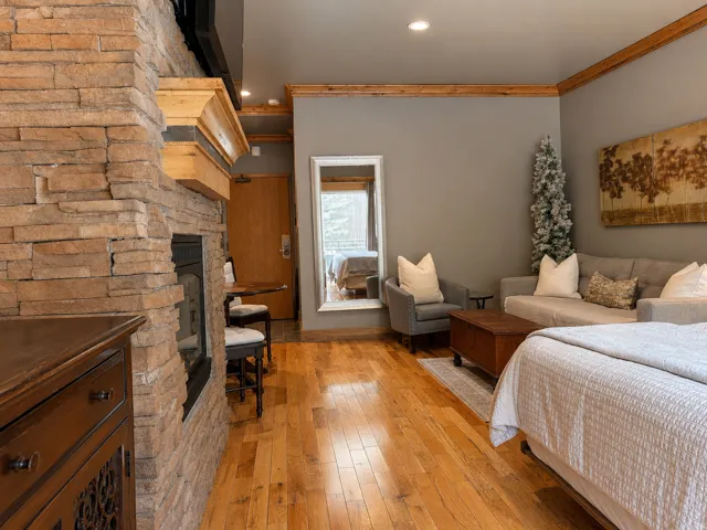 Stone-clad fireplace with a wood mantle, hardwood flooring, wood-finish trim, a recessed ceiling light, and a wood entry door