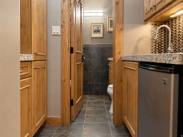 Wood-finish cabinetry with granite countertops, a built-in stainless steel mini-refrigerator, and a mosaic tile backsplash
