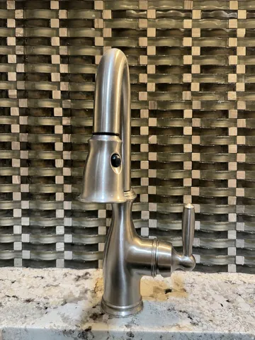 Brushed nickel faucet with a pull-down sprayer, single lever handle, and a backsplash featuring a woven glass tile pattern