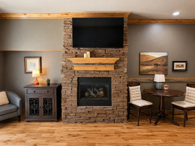 Stacked stone fireplace with a wood mantel, wood-finish flooring, and built-in crown molding