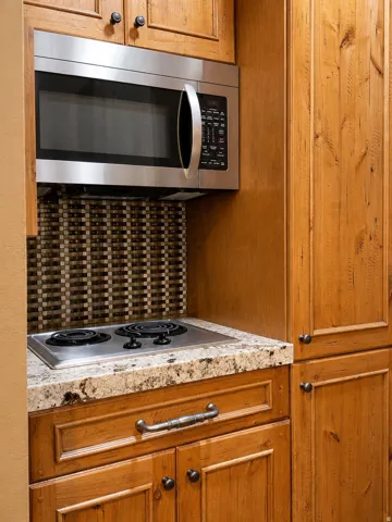 Built-in stainless steel microwave, integrated two-burner cooktop, stone-finish countertop, wood cabinetry, and mosaic tile backsplash