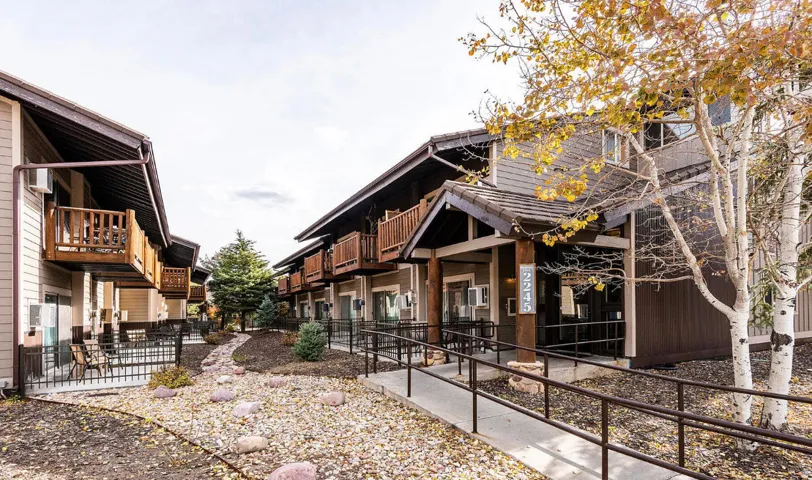 Wood siding exterior, multiple balconies, ground-level patios, paved walkway with handrails, and a decorative rock landscape