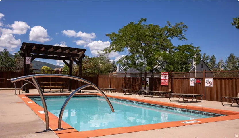 Rectangular swimming pool with integrated entry handrails, concrete surround, and a dark wood pergola