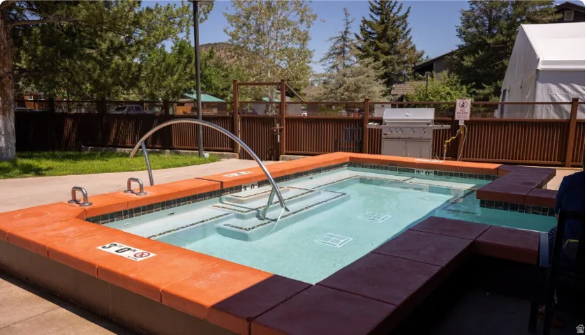 Swimming pool with integrated steps and stainless steel handrails, surrounded by a concrete patio and wood fencing