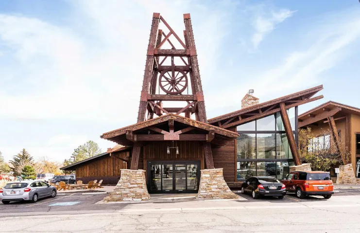 Facade featuring a rustic wood and stone exterior, prominent wood-beam tower, large glass window panels, and a stone chimney
