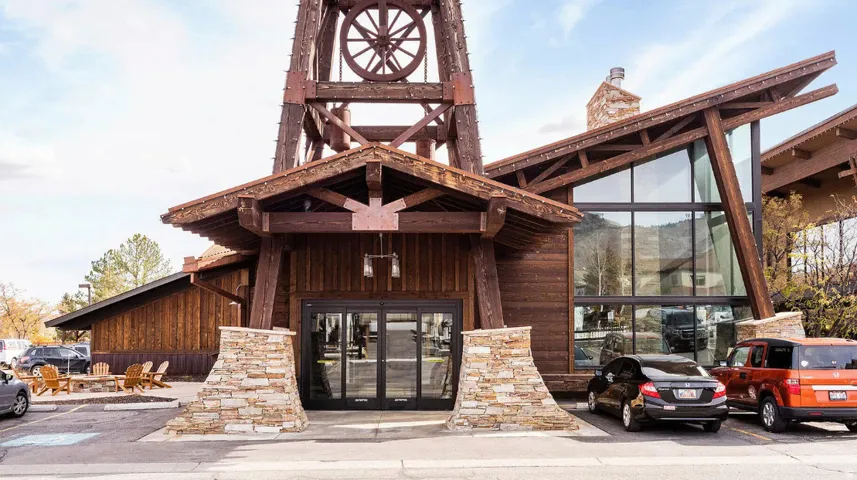 Timber-frame facade with stacked stone accents, expansive glass curtain wall, and a prominent decorative wheel structure