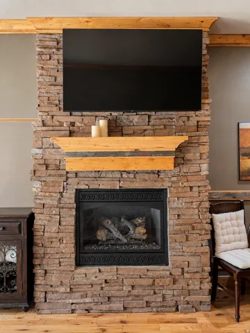 Stone-clad fireplace with a natural wood mantel and gas log insert